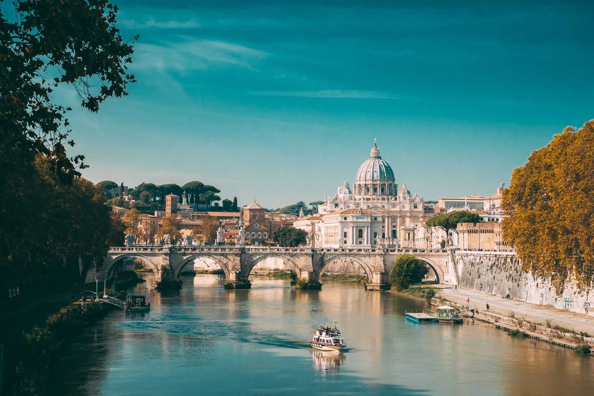 View of the Tiber river with St. Peter Basilica in the background during sunny day in Rome