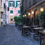 A narrow cobbled street in Trastevere lined with outdoor tables and lanterns