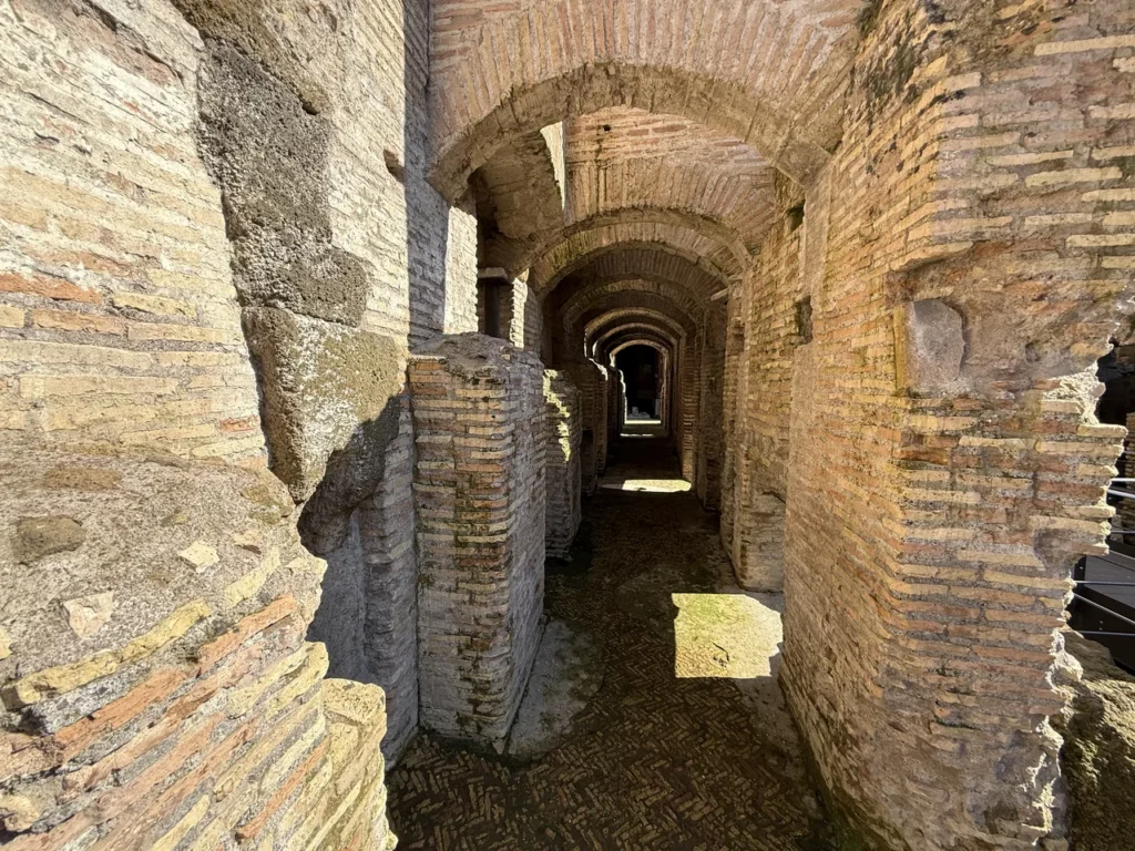 A warm brick-vaulted underground corridor in ancient Rome receding into shadow