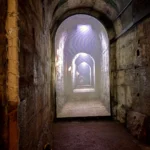 An arched underground tunnel beneath Rome, lit at the far end